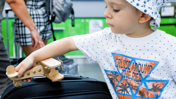 Closeup photo of little boy with big suitcase and toy wooden airplane in airport terminal — Stock Photo, Image