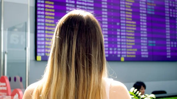 Образ молодой женщины, ищущей время полета на большом дисплее в терминале аэропорта — стоковое фото