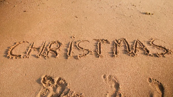 Kép a szót karácsony írt a homok a tengerparton. Téli ünnepek, szilveszteri és idegenforgalmi koncepció — Stock Fotó