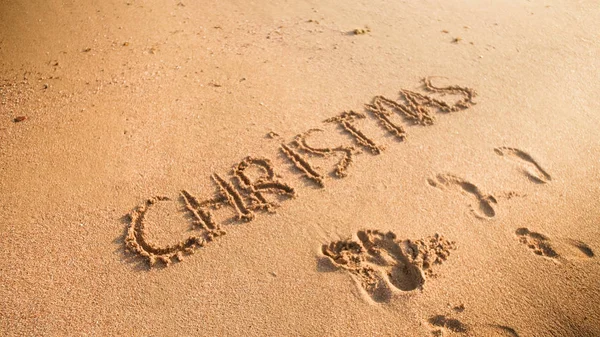 Close-up beeld van Kerstmis inscripted woord aan zandstrand. Footaprints op nat zand. Concept van wintervakantie, Nieuwjaar en toerisme — Stockfoto