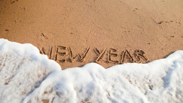 Closeup photo of sea waves rolling over words New Year written on wet sand on the beach. Concept of winter holidays, Christmas and tourism — Stock Photo, Image