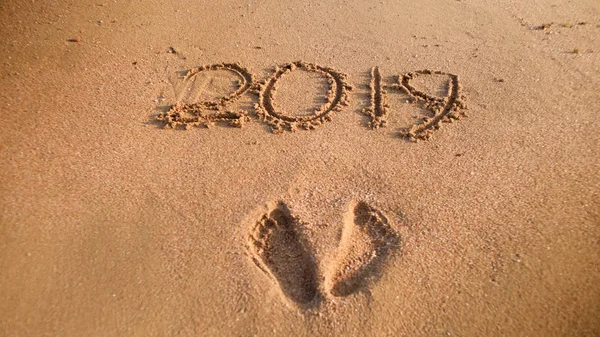 Närbild bild av fotspår och 2019 nummer skrivna på våt sand vid havet stranden. Koncept för nyår, jul och resor på vintern helgdagar. — Stockfoto