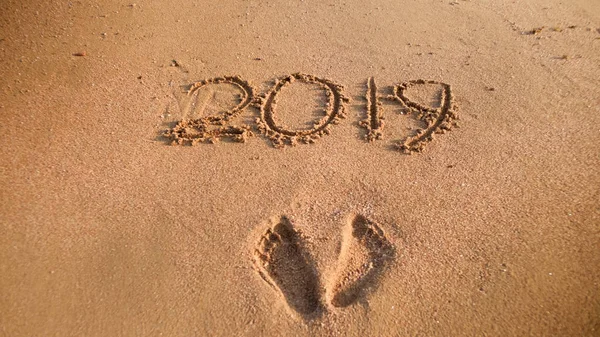 Närbild foto av 2019 nya året nummer och footrpints på våt sand på Ocean Beach. Koncept för nyår, jul och resor på vintern helgdagar. — Stockfoto