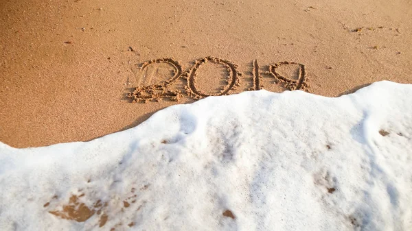 Närbild foto av havsvågor rullande över 2019 nummer skrivna på våt sand på stranden. Koncept för nyår, jul och resor på vintern helgdagar. — Stockfoto