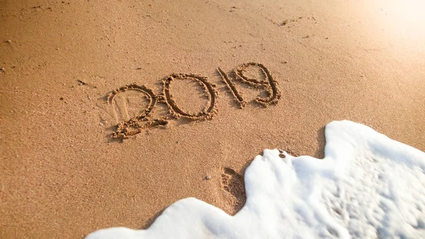 Närbild foto av havet våg rullande över 2019 nummer skrivna på våt sand. Koncept för nyår, jul och resor på vintern helgdagar. — Stockfoto