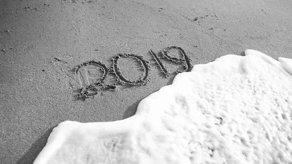 Zwart-wit beeld van 2019 Nieuwjaar nummers geschreven op zee strand. Concept van vieringen, kerst en reizen op wintervakantie. — Stockfoto