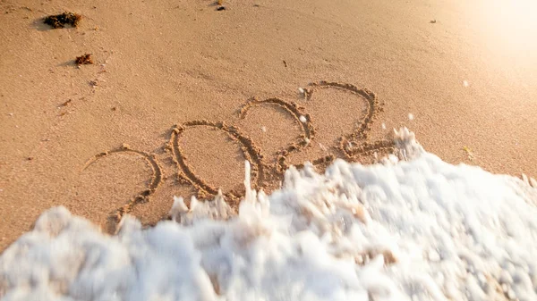 Closeup photo of ocean wave rolling over 2022 New Year numbers written on wet sand at island beach. Concept of New Year, Christmas and travel on winter holidays. — Stock Photo, Image