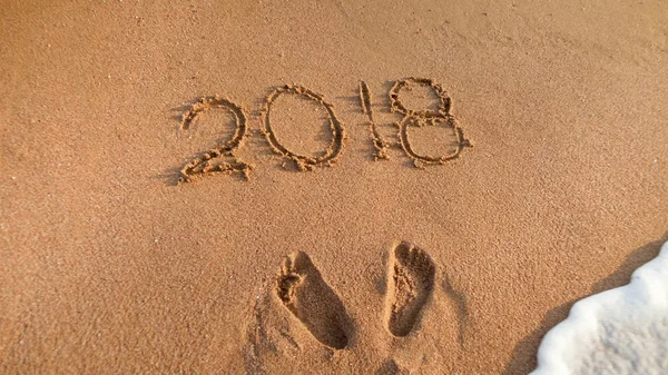 Närbild bild av fotspår och 2018 tal skrivna på våta strand sand — Stockfoto