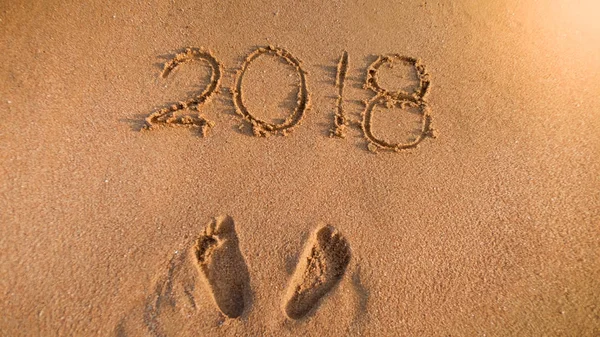 Närbild bild o Footprints bredvid 2018 Ne år nummer skrivna på Wet Beach sand. Perfekt bild för att illustrera jul, vintersemester, resor och turism. — Stockfoto