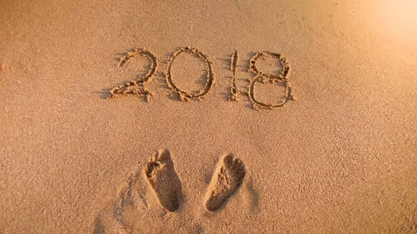 2018 siffror och personer fotavtryck på våt havet strand sand. Koncept för att fira och resa på sportlov. — Stockfoto