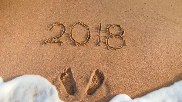 Close-up foto van zee golven rollen over 2018 Nieuwjaar nummers geschreven op zand. Concept van vieren en reizen op Winter vakantie. — Stockfoto
