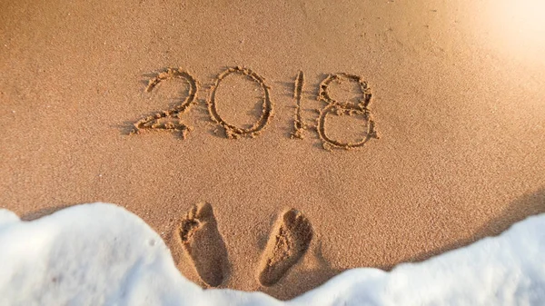 Närbild foto av två fotspår och 2018 nummer skrivna på Wet Beach sand. Koncept för att fira och resa på sportlov. — Stockfoto