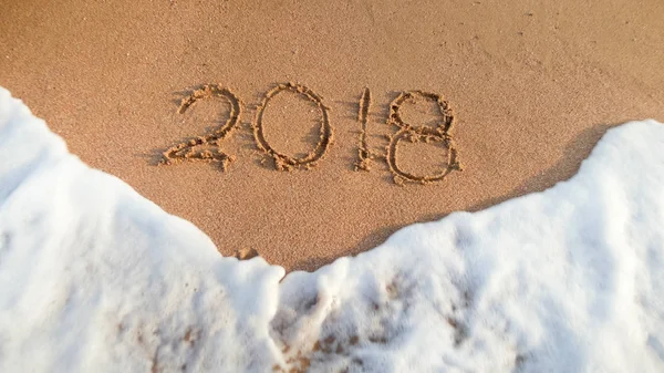 Närbild foto av havsvågor rullande över 2018 siffror skrivna på våt sand. Koncept för att fira och resa på sportlov. — Stockfoto