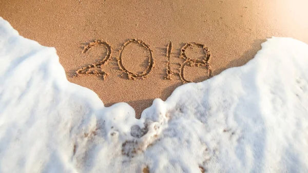 Närbild foto av Ocean Waves tvätta bort 2018 nummer skrivna på våt sand. Koncept för att fira och resa på sportlov. — Stockfoto