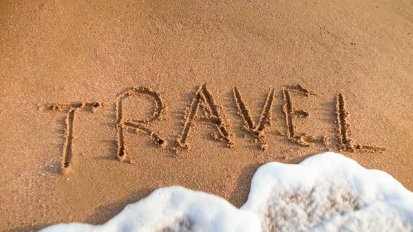 Imagen de cerca de las olas del mar lavando la palabra Viaje escrito en la arena de la playa. Concepto de turismo, viajes, viajes y viajes . — Foto de Stock