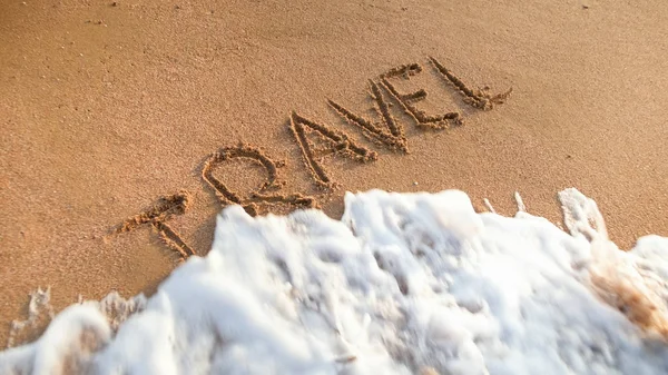 Foto de primer plano de las olas del océano rodando sobre los viajes de palabras escritas en arena mojada. Concepto de turismo, viajes, viajes y viajes . — Foto de Stock