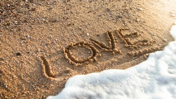 Closeup photo of ocean waves washing off word Love written on wet sand — Stock Photo, Image