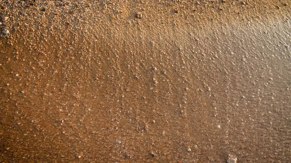 Крупный план текстуры влажного песка и мелких скал на пляже на закате — стоковое фото