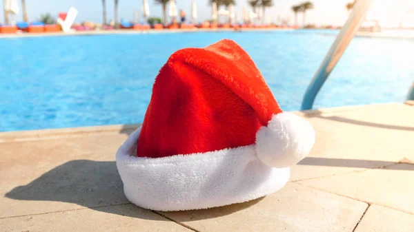 Image rapprochée du chapeau de Santas couché au bord de la piscine. Concept de voyage et de tourisme à Noël, Nouvel An et vacances d'hiver . — Photo