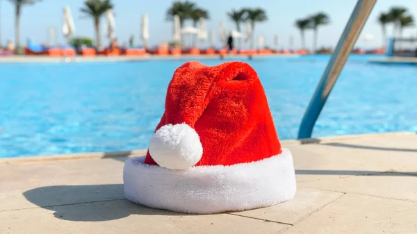 Imagem do boné vermelho do Papai Noel situado ao lado da piscina no resort de verão. Conceito de viagem e turismo no Natal, Ano Novo e férias de inverno . — Fotografia de Stock