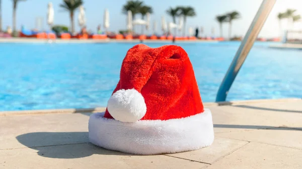 Imagem de close-up do chapéu vermelho de Papai Noel deitado ao lado da piscina no resort ilha. Conceito de viagem e turismo no Natal, Ano Novo e férias de inverno . — Fotografia de Stock