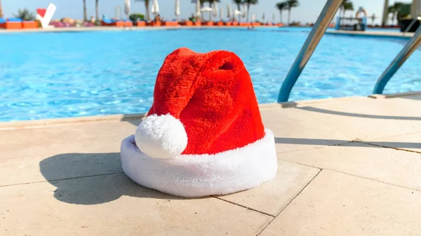 Immagine del berretto Snta rosso che giace a bordo piscina nella località estiva. Concetto di viaggio e turismo a Natale, Capodanno e vacanze invernali . — Foto Stock