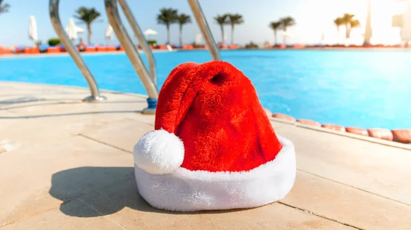 Foto de close-up do chapéu de Papai Noel deitado à beira da piscina no resort de verão. Conceito de viagem e turismo no Natal, Ano Novo e férias de inverno . — Fotografia de Stock