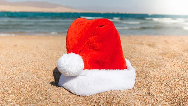 Photo rapprochée du Père Noël a laissé son chapeau sur la plage de sable à la mer. Concept de voyage et de tourisme à Noël, Nouvel An et vacances d'hiver . — Photo