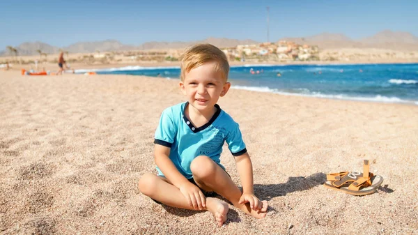 Portret cute trzy lata chłopiec maluch siedzi na piaszczystej plaży na morzu. — Zdjęcie stockowe