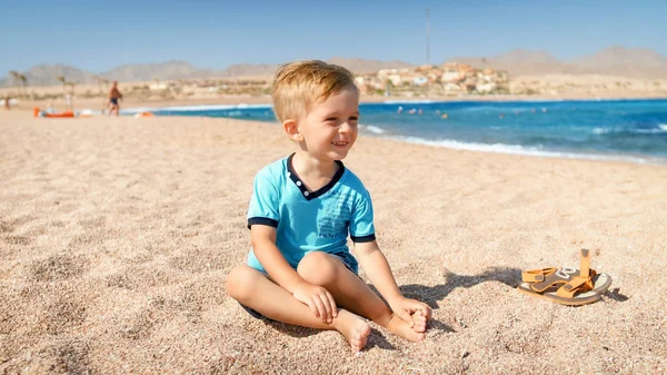Portret szczęśliwego śmiechu chłopca siedzącego na plaży morskiej w jasnym, słonecznym dniu. — Zdjęcie stockowe