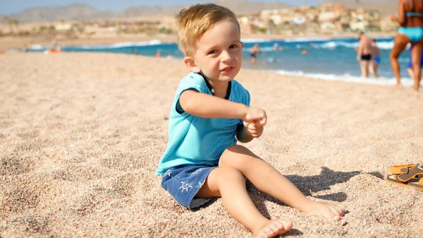 Śmieszne maluch chłopiec siedzi na piasku na plaży i taniec — Zdjęcie stockowe