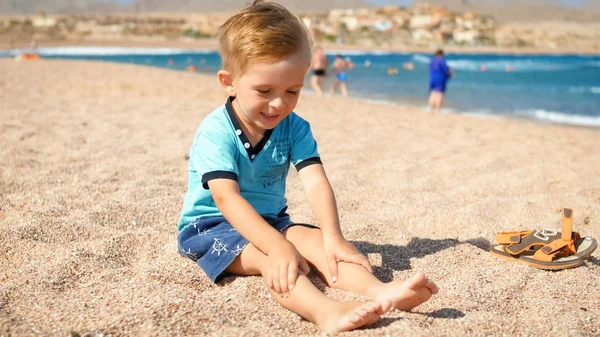 Cute Little Boy siedzi na plaży na morzu i patrząc na jego nogi — Zdjęcie stockowe