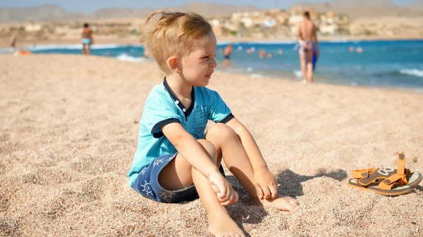 Portret zdenerwowany chłopiec maluch siedzi na piasku na plaży morskiej — Zdjęcie stockowe