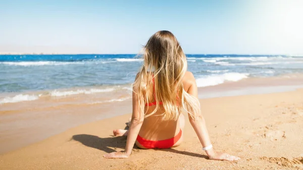 Rera view photo of beautiful young woman in red bikini relaxing on the beach and looking at horizon — Stock Photo, Image