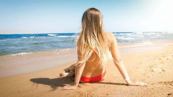Rear view photo of beautiful young woman with long hair relaxing on beach at windy sunny day — Stock Photo, Image
