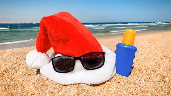 Foto de close-up de chapéu de Santas e óculos de sol na praia do mar. Conceito de viagem e turismo no Natal, Ano Novo e férias de inverno . — Fotografia de Stock