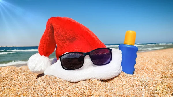 Close-up foto van Santas hoed en zonnebril op het strand. Concept van reizen en toerisme op Kerstmis, Nieuwjaar en wintervakantie. — Stockfoto