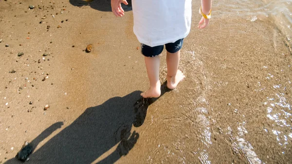 Image rapprochée d'un petit garçon debout sur une plage de sable mouillé à la mer — Photo