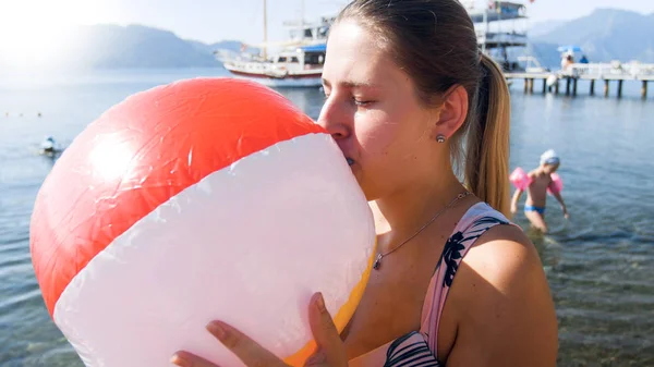 Potret wanita cantik muda dengan pakaian renang meniup bola pantai yang dapat digulung di laut — Stok Foto