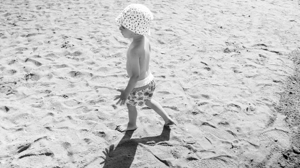 Black and white image of little toddler boy walking on hot sand at sea beach — Stock Photo, Image
