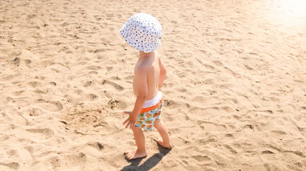 Mały maluch chłopiec w białym kapeluszu chodzenie na piaszczystej plaży — Zdjęcie stockowe