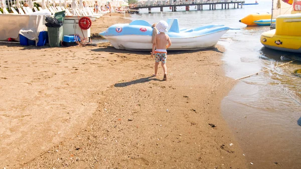Rera view image of little toddler boy walking on sea beach toward boats and catamarans — Stock Photo, Image