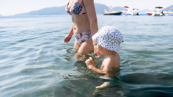 Netter kleiner Junge, der mit seiner jungen Mutter im Meer spazieren geht — Stockfoto