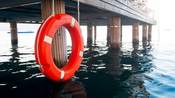 Closeup image of orange lifesaving buoy hanging on long wooden pier at sea beach — Stock Photo, Image