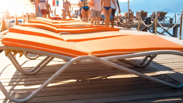 Imagen borrosa de turistas caminando junto a tumbonas vacías en el muelle de madera en la playa del mar —  Fotos de Stock