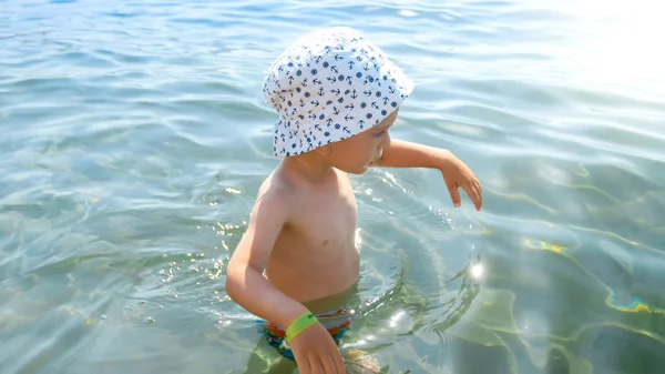 Pequeño niño pequeño con sombrero caminando en el mar en el día soleado caliente — Foto de Stock