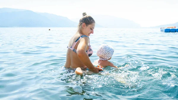 Kleiner Kleinkind-Junge schwimmt an heißen Sommertagen mit seiner jungen lächelnden Mutter im Meer — Stockfoto