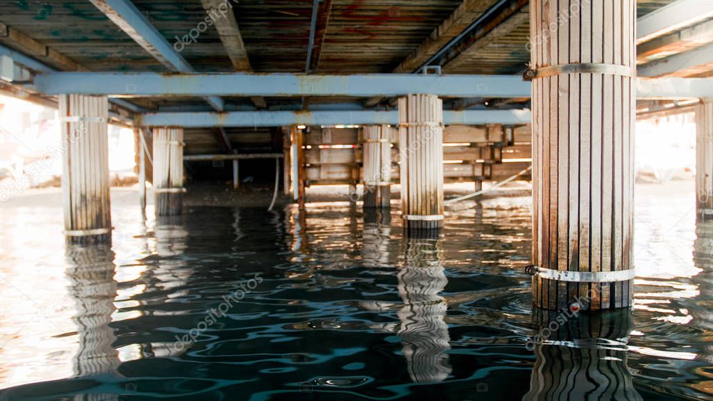 Image of sea waves and wooden colums under pier at sea shore