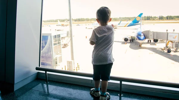 Imagem tonificada do menino criança olhando em aviões na pista no terminal do aeroporto — Fotografia de Stock