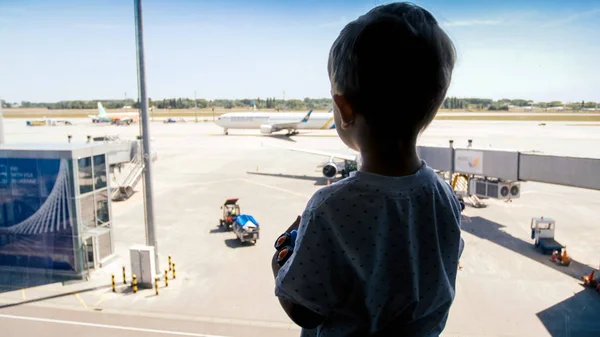 Silhueta de menino olhando em aviões de aterrissagem no aeroporto através de grande janela — Fotografia de Stock